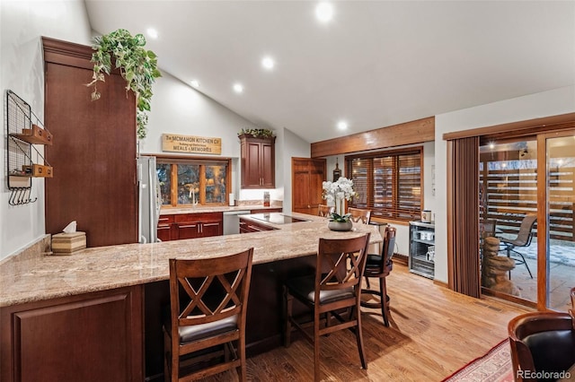 kitchen with light stone countertops, light wood finished floors, a peninsula, vaulted ceiling, and appliances with stainless steel finishes