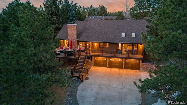 view of front of property featuring a deck, concrete driveway, an attached garage, a shingled roof, and stairs