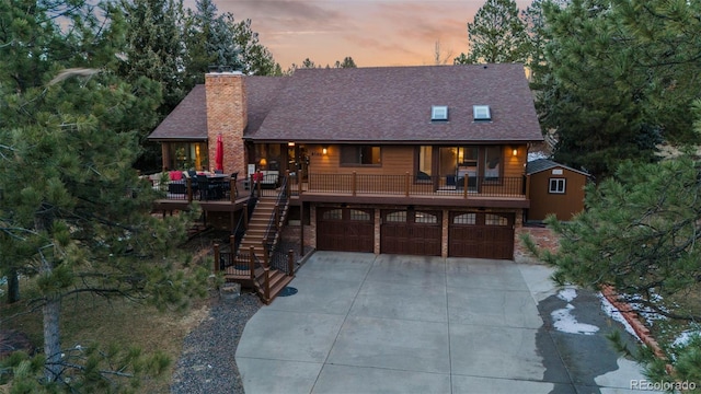 chalet / cabin featuring stairway, roof with shingles, a chimney, a garage, and driveway