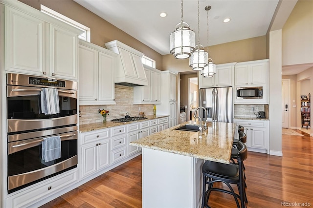 12121 Bryant St, Westminster, CO 80234 - kitchen with appliances with stainless steel finishes, premium range hood, decorative backsplash, a center island with sink, and white cabinets
