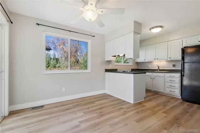 kitchen with black fridge, kitchen peninsula, ceiling fan, light wood-type flooring, and white cabinetry