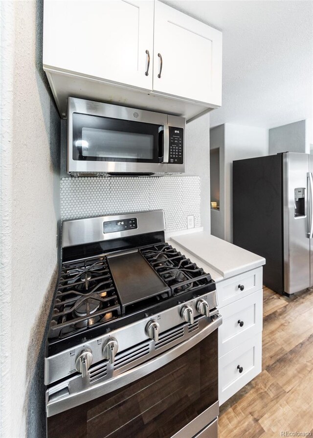 1726 E Evans Ave, Pueblo, CO 81004 - kitchen with appliances with stainless steel finishes, white cabinetry, light wood-style floors, backsplash, and light countertops