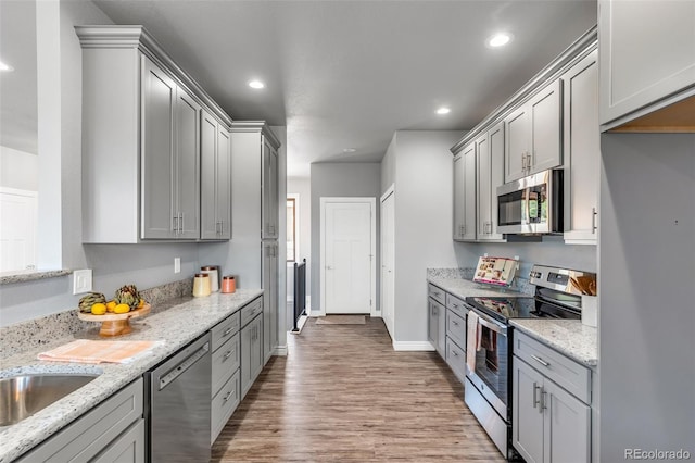 kitchen with gray cabinets, appliances with stainless steel finishes, light stone counters, and light hardwood / wood-style floors