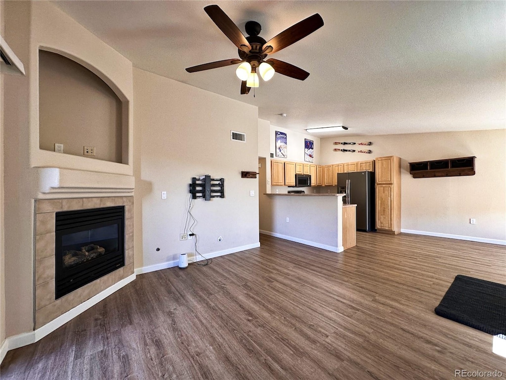 unfurnished living room featuring a tiled fireplace, dark hardwood / wood-style flooring, vaulted ceiling, a textured ceiling, and ceiling fan