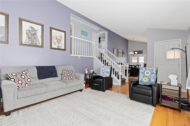 living area with an inviting chandelier, stairway, vaulted ceiling, and wood finished floors