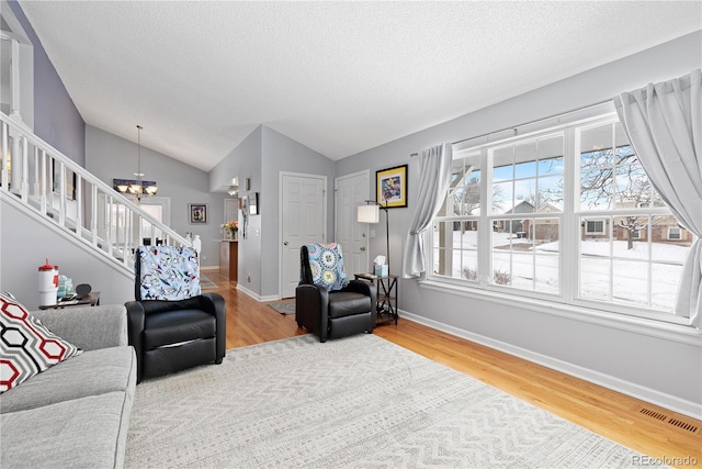 living area featuring a notable chandelier, wood finished floors, baseboards, stairs, and vaulted ceiling