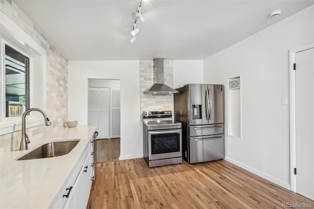 6170 Estes Ct, Arvada, CO 80004 - kitchen featuring wall chimney range hood, decorative backsplash, a sink, white cabinets, and stainless steel appliances