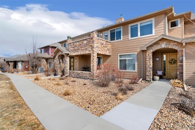 view of front of home featuring a balcony, stone siding, and central AC