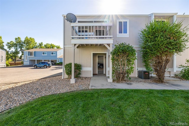 view of front of home featuring a balcony, a front lawn, and central AC