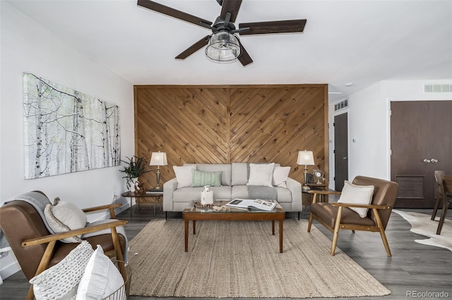 living room featuring wood-type flooring, wooden walls, and ceiling fan