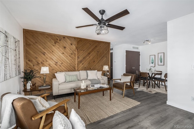 living room with wood walls, dark wood-type flooring, and ceiling fan