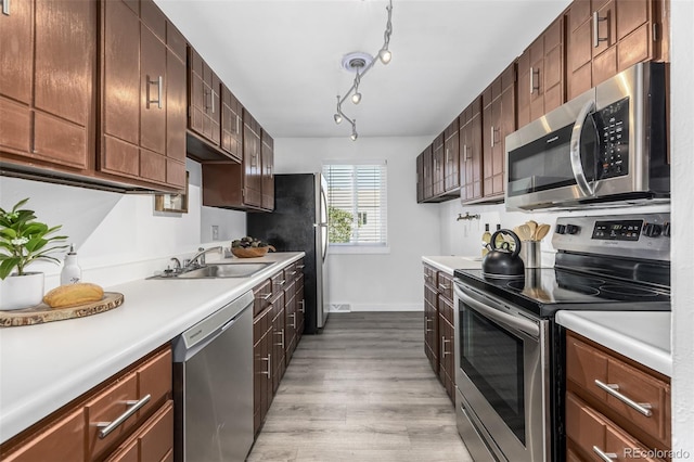 kitchen with dark brown cabinetry, sink, rail lighting, stainless steel appliances, and light wood-type flooring