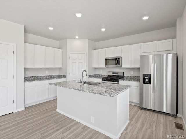 1134 Thunder Pass Rd, Severance, CO 80550 - kitchen with stainless steel appliances, light wood-style flooring, white cabinetry, a center island with sink, and light stone countertops
