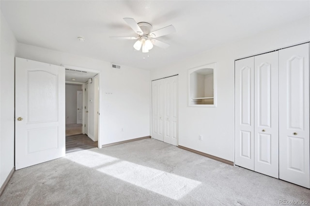 unfurnished bedroom featuring visible vents, baseboards, ceiling fan, light colored carpet, and two closets