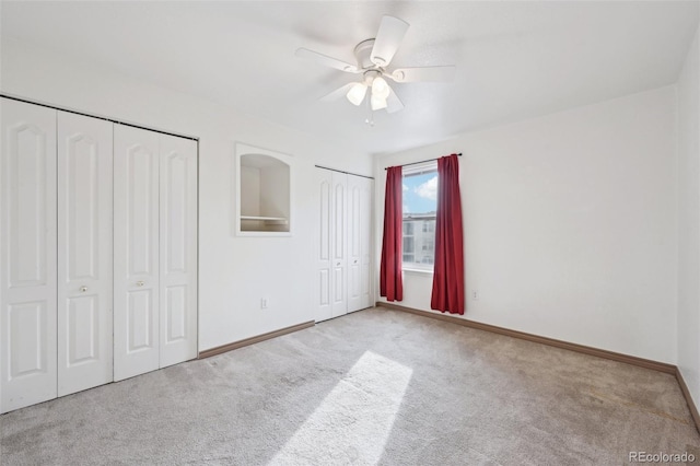 unfurnished bedroom with a ceiling fan, carpet flooring, baseboards, and multiple closets