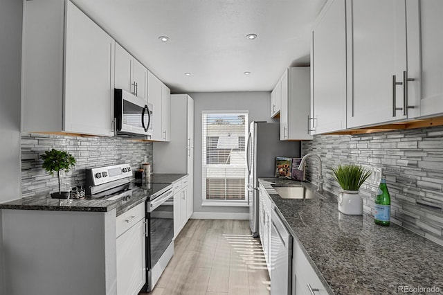 kitchen featuring stainless steel appliances, white cabinetry, dark stone counters, and sink