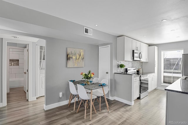 kitchen with white cabinetry, stainless steel appliances, tasteful backsplash, dark stone countertops, and light wood-type flooring