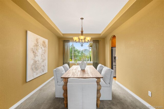 carpeted dining room featuring a chandelier, a textured wall, arched walkways, baseboards, and a tray ceiling