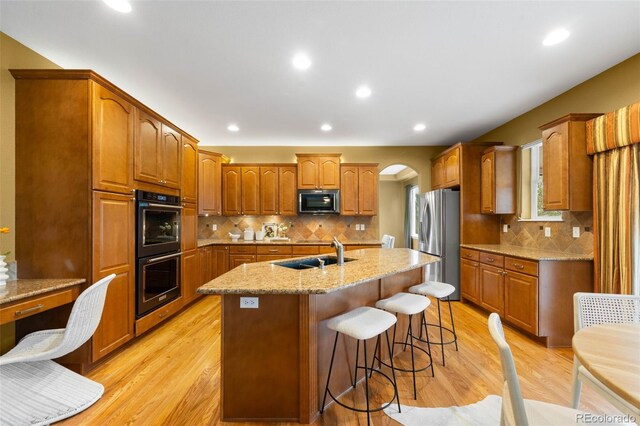 kitchen featuring a sink, appliances with stainless steel finishes, brown cabinets, a center island with sink, and recessed lighting
