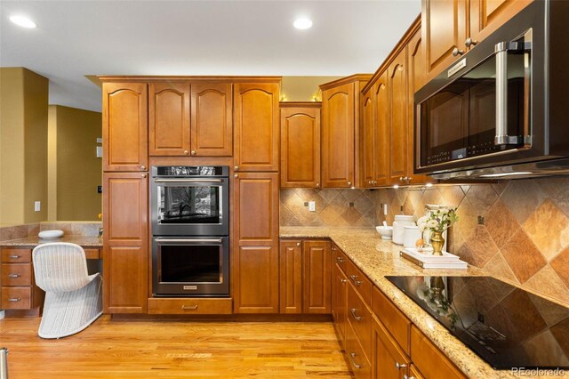 kitchen with double wall oven, black electric cooktop, light stone countertops, light wood-type flooring, and recessed lighting