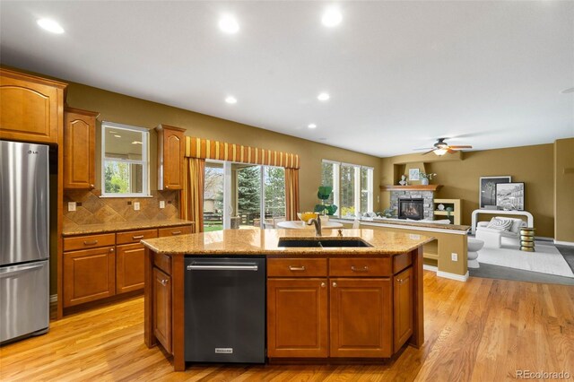 kitchen with appliances with stainless steel finishes, a sink, a center island with sink, a fireplace, and ceiling fan
