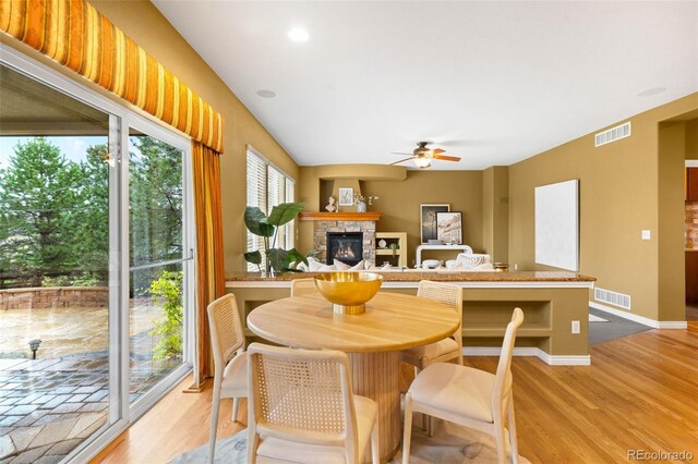 dining space featuring a ceiling fan, a stone fireplace, light wood-style flooring, recessed lighting, and baseboards