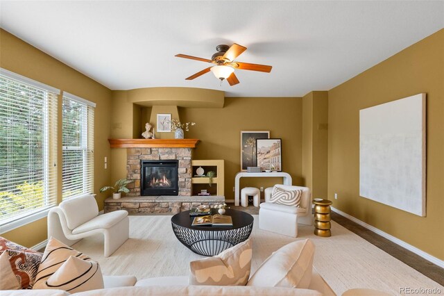 carpeted living room featuring baseboards, ceiling fan, and a stone fireplace