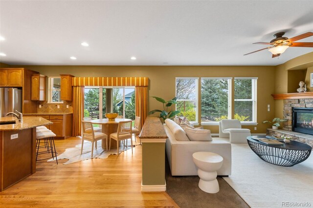 living room featuring light wood-style flooring, a stone fireplace, recessed lighting, and a ceiling fan