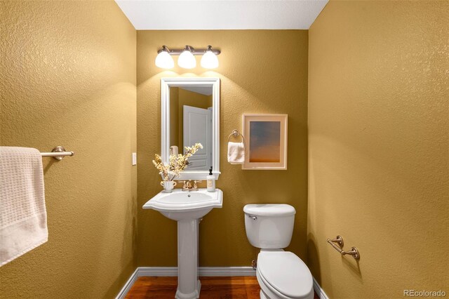 bathroom with toilet, baseboards, and wood finished floors