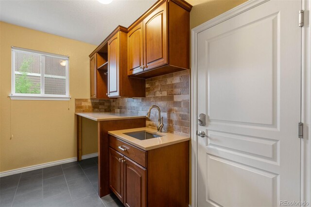 kitchen with a sink, tasteful backsplash, baseboards, light countertops, and dark tile patterned flooring