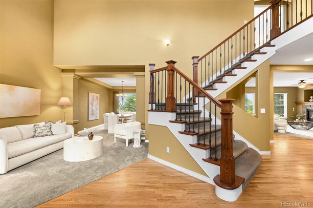 living room with a towering ceiling, wood finished floors, healthy amount of natural light, stairs, and a chandelier