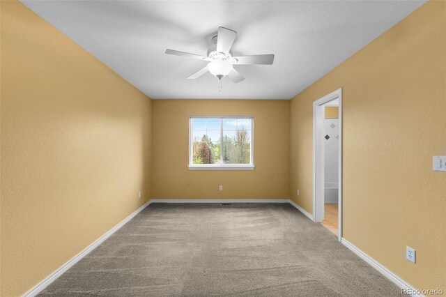 empty room with carpet flooring, ceiling fan, baseboards, and a textured wall