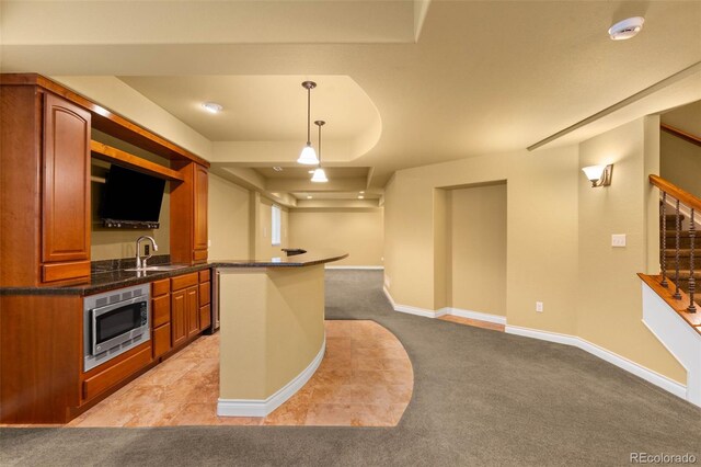kitchen with stainless steel microwave, light colored carpet, a sink, brown cabinetry, and hanging light fixtures