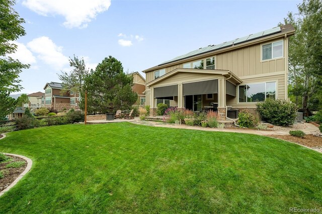 rear view of property featuring roof mounted solar panels, a yard, a patio area, and board and batten siding
