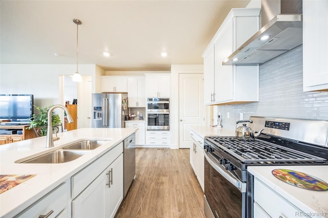 kitchen featuring wall chimney exhaust hood, sink, white cabinetry, decorative light fixtures, and stainless steel appliances