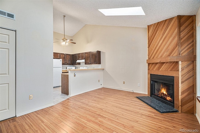 unfurnished living room featuring a skylight, ceiling fan, a large fireplace, light hardwood / wood-style floors, and a textured ceiling