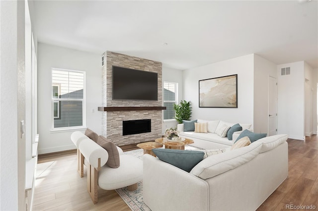 living area featuring a wealth of natural light, a stone fireplace, visible vents, and light wood-style flooring