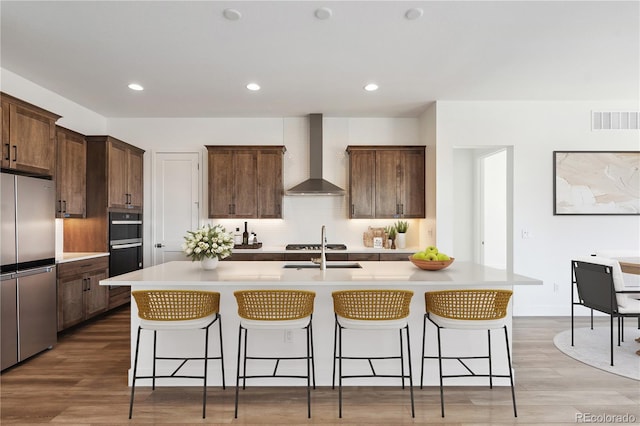 kitchen with light countertops, wall chimney range hood, stainless steel refrigerator, and a kitchen island with sink