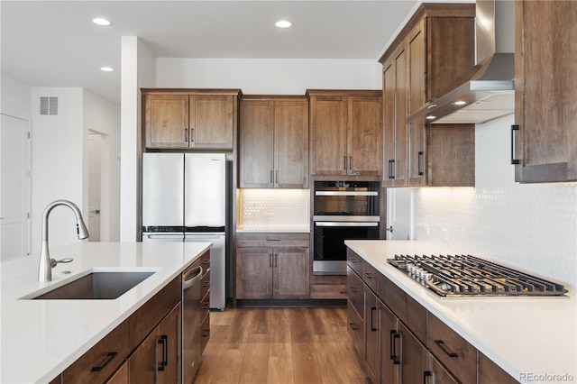 kitchen with visible vents, wall chimney exhaust hood, appliances with stainless steel finishes, light countertops, and a sink