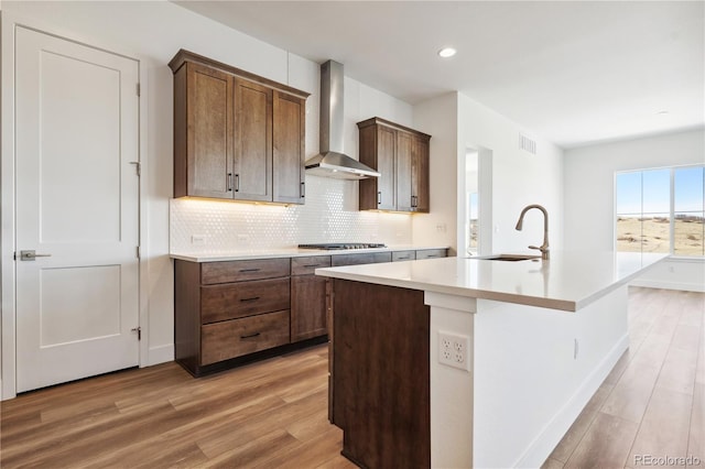 kitchen featuring light countertops, visible vents, a kitchen island with sink, a sink, and wall chimney range hood