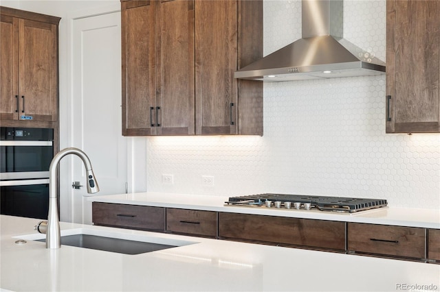 kitchen with decorative backsplash, wall chimney exhaust hood, light countertops, stainless steel gas stovetop, and a sink