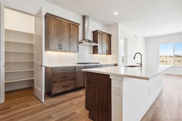 kitchen featuring visible vents, light countertops, a sink, an island with sink, and wall chimney exhaust hood