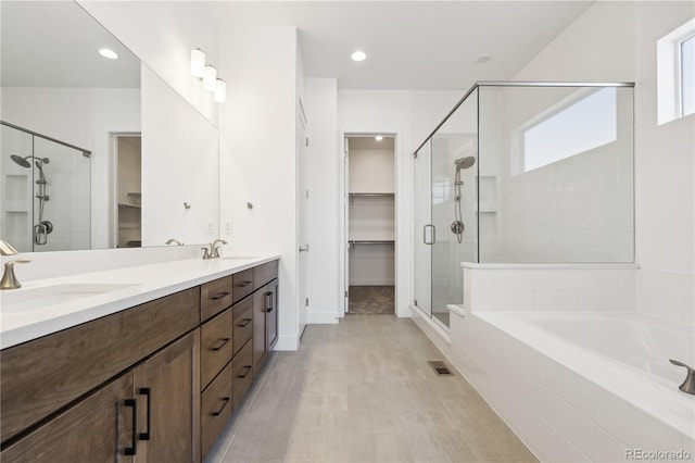 bathroom featuring a walk in closet, a sink, a shower stall, and double vanity