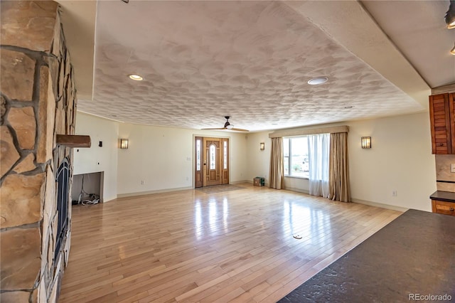 empty room with a fireplace, a textured ceiling, ceiling fan, and light hardwood / wood-style floors