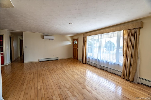 unfurnished room with a baseboard heating unit, a wall unit AC, and light hardwood / wood-style floors