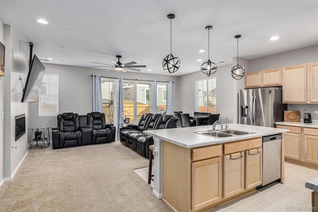 kitchen with stainless steel appliances, an island with sink, light brown cabinetry, sink, and decorative light fixtures