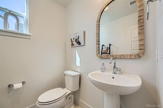 half bath featuring visible vents, a sink, toilet, and baseboards