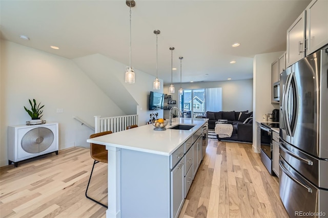 kitchen featuring stainless steel appliances, light wood-style floors, open floor plan, a sink, and a kitchen bar