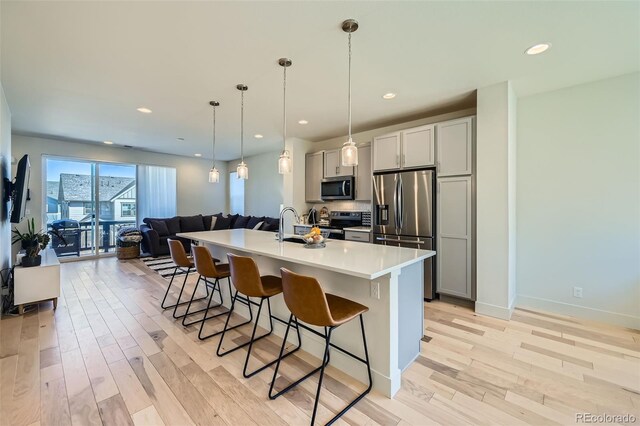 kitchen featuring a breakfast bar, light countertops, light wood-style flooring, appliances with stainless steel finishes, and open floor plan