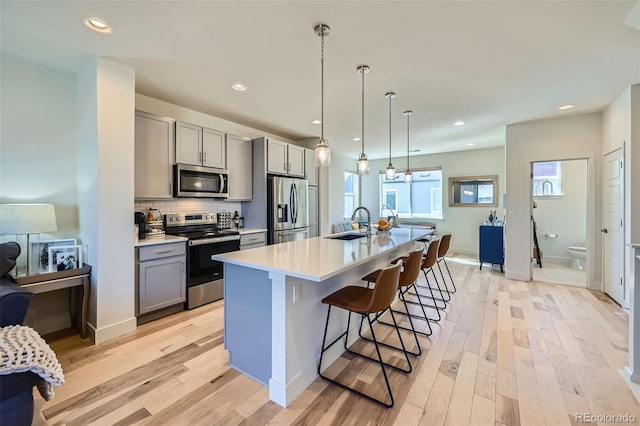 kitchen with light wood finished floors, tasteful backsplash, appliances with stainless steel finishes, gray cabinetry, and a sink